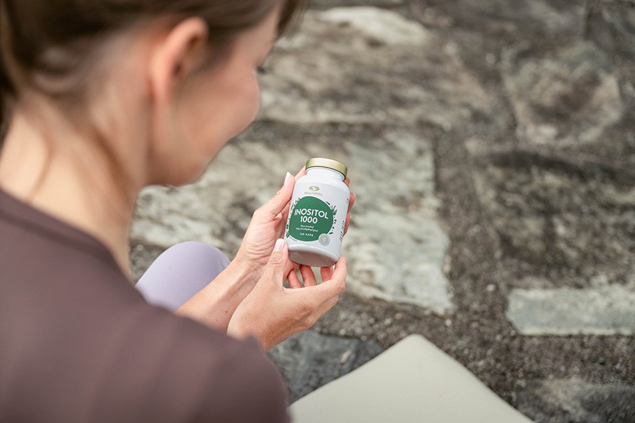 Kvinde sidder på en yogamåtte og holdedr en bøtte Healthwell Inositol 1000 i hænderne.