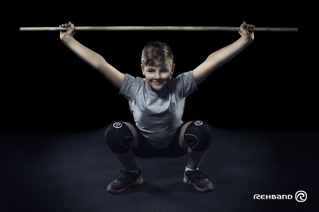 Dreng udfrer en overhead squat med vgtstang og Rehbands knbeskytter.