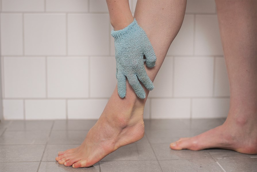 Hnd med skrubbehandske, der peeler et ben