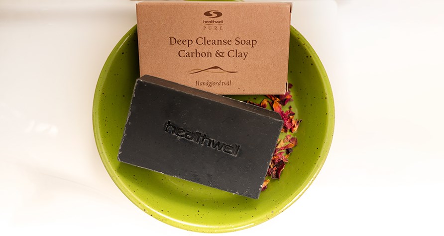 Healthwell PURE Deep Cleanse Soap Carbon & Clay placeret i grn stenskl med trrede rosenblade.