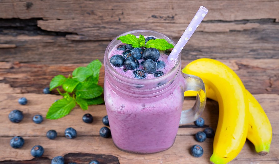 En blbrssmoothie str p et bord omringet af blbr og en banan.