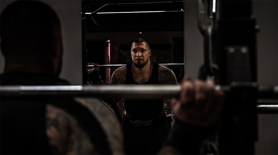 En mand i tr�ningsmilj� foran et spejl g�r sig klar til at lave en kn�b�j med stang.