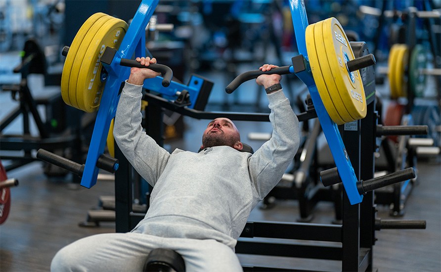 En mand laver bnkpres p en maskine i et fitnesscenter.