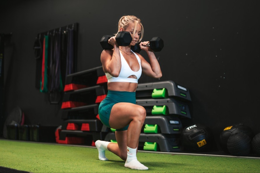 Denice Moberg laver lunges med hndvgte i et fitness center.