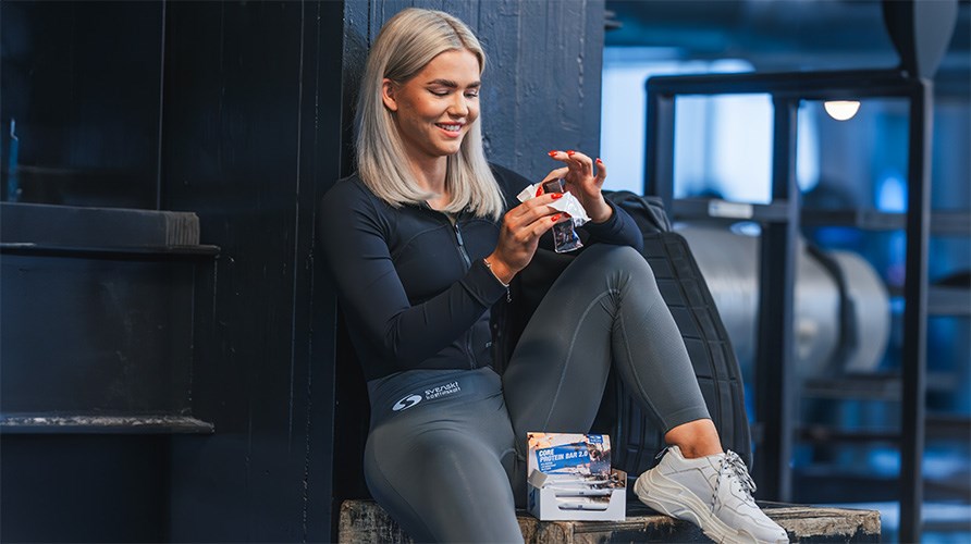 Billede af Fiddelie i fitnesscenteret, mens hun spiser en proteinbar.