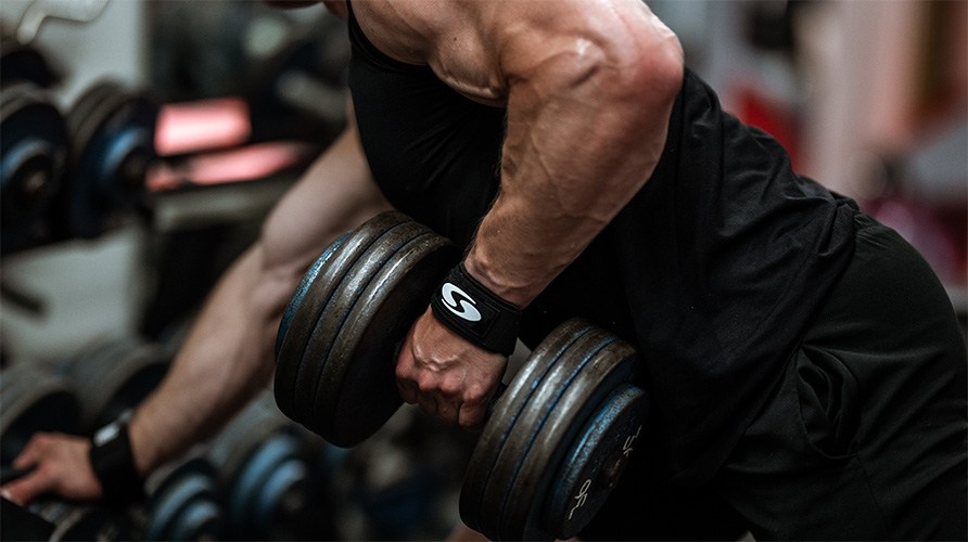 En muskuls mand laver en-armetroning med en hndvgt i et trningscenter.