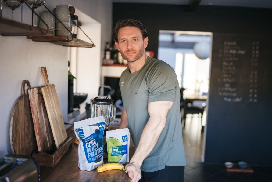 Kenneth str i et kkken foran en blender, Core Whey Protein og Core Green Boost.