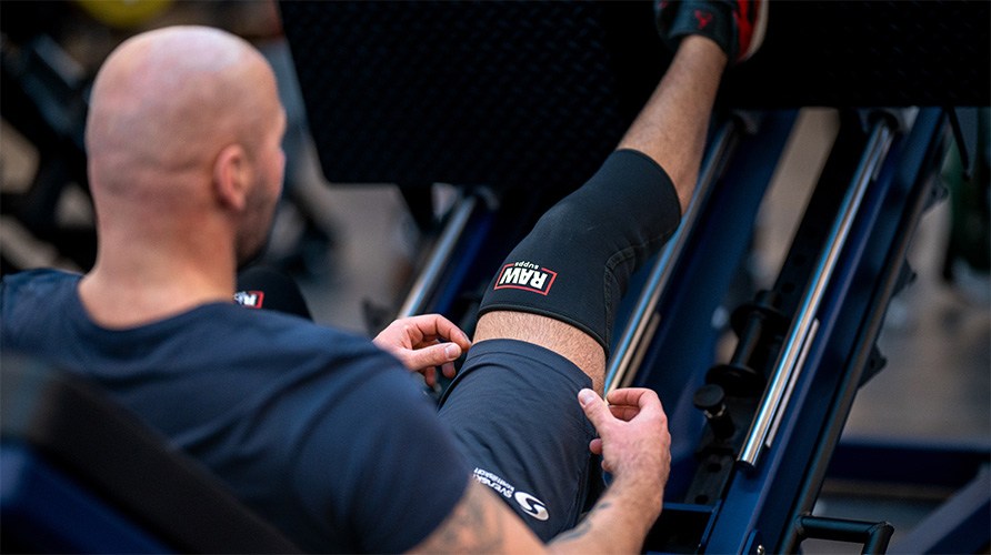 En mand laver en-benet benpress med knæbeskyttere på. En mand laver en-benet benpress med knæbeskyttere på.