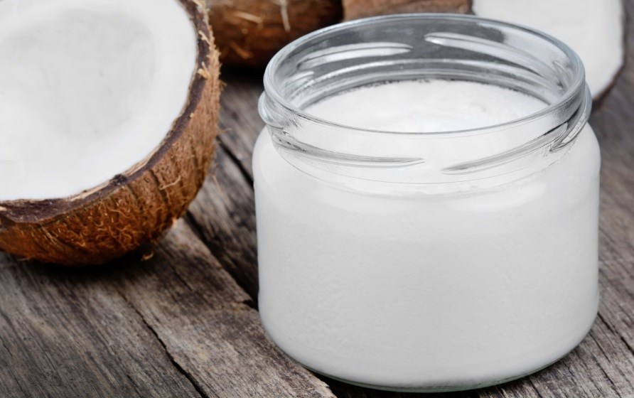 Kokosolie i glas med en halv kokos ved siden af. Kokosolie i glas med en halv kokos ved siden af.