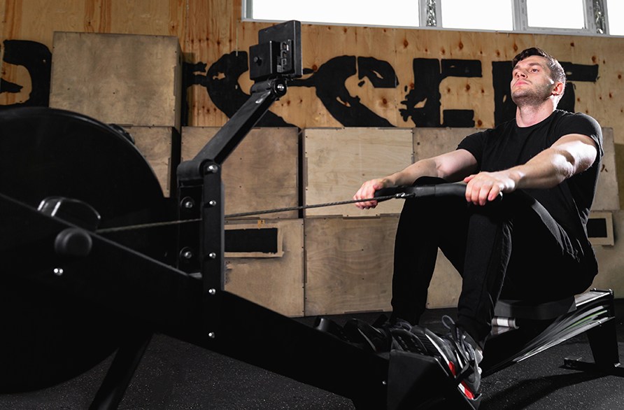 En mand sidder i en romaskine og trner, i et trningscenter.