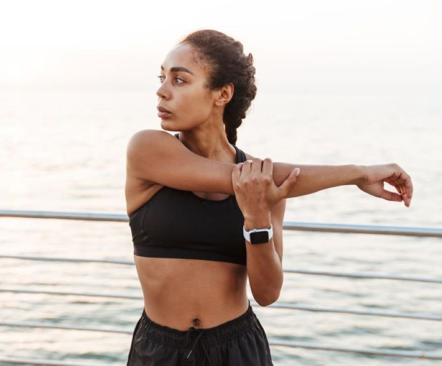 Kvinde i trningstj der strkker sin arm i et udendrsmilj.