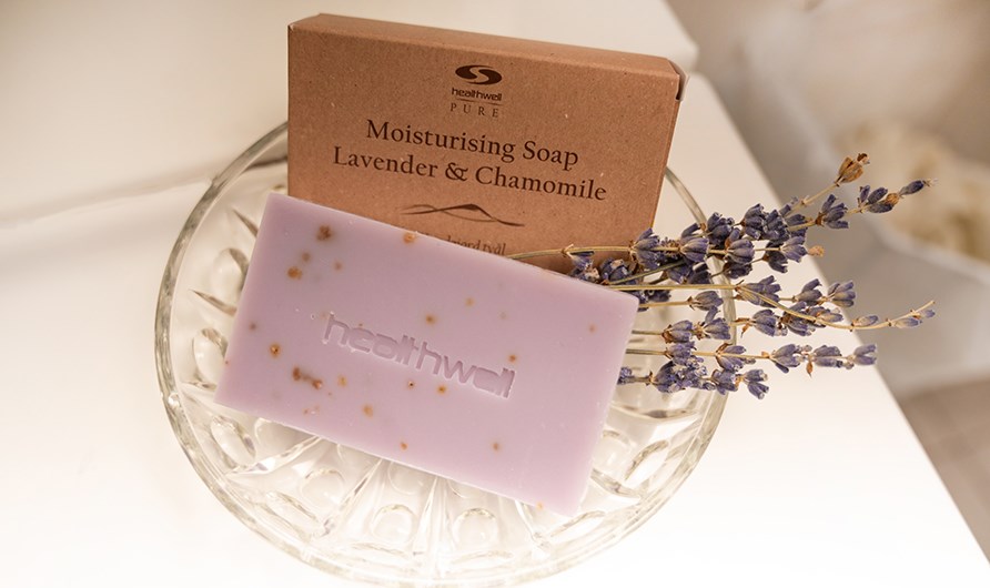 Healthwell PURE Moisturising Soap Lavender & Chamomile i glasskl med lilla trret lavendel.