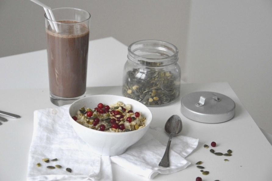 En skl med proteingrd toppet med grskarkerner og tyttebr str p et bord.