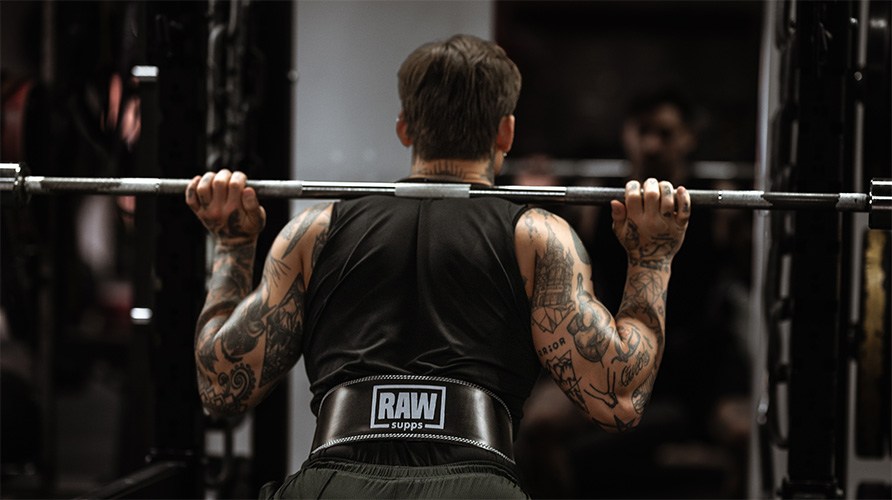 En mand med et lfteblte str parat til at udfre squat med stang p ryggen.