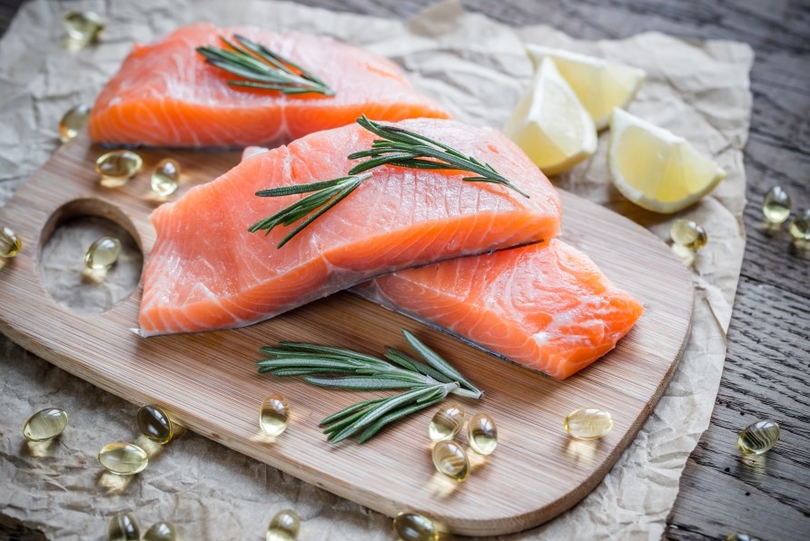Tre laksefileter på et skærebræt sammen med omega-3 kapsler og citronskiver. Tre laksefileter på et skærebræt sammen med omega-3 kapsler og citronskiver.