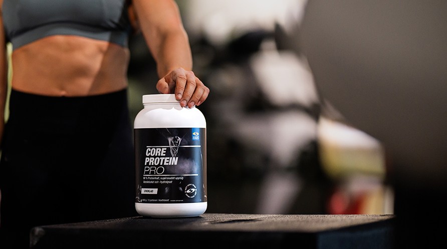 En kvinde i et trningscenter str med hnden p en btte Core Protein Pro.