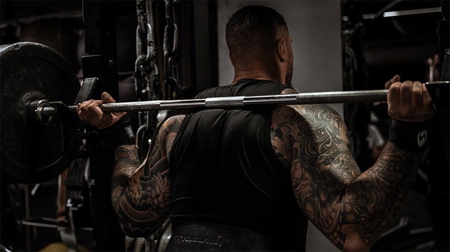 En mand med muskuls ryg str ved en vgtstang.