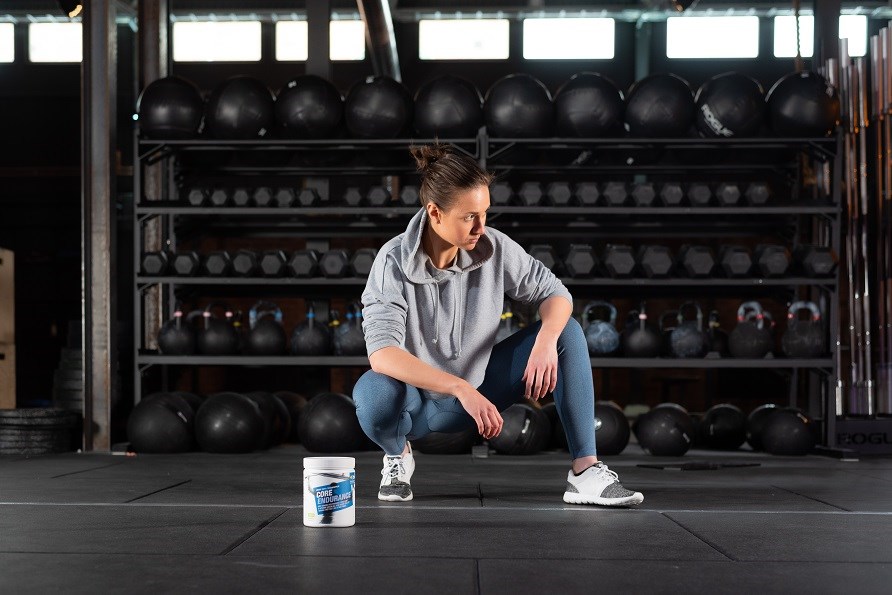 En pige sidder p gulvet i et fitnesscenter med en btte Core Endurance.