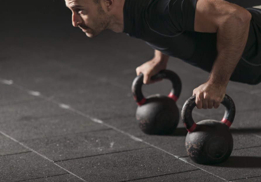 En mand laver armbjninger p to kettlebells.