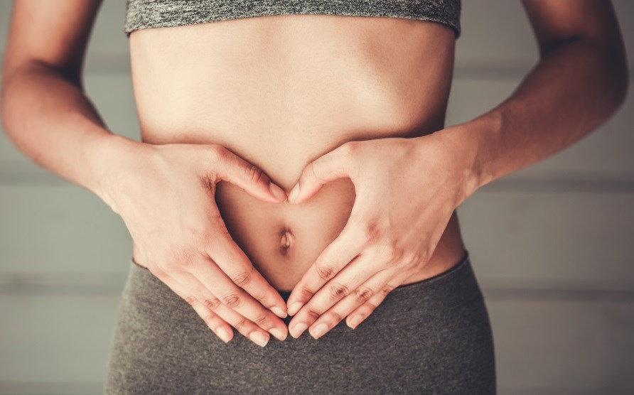 En kvinde holder sig på maven med hænderne formet som et hjerte. En kvinde holder sig på maven med hænderne formet som et hjerte.