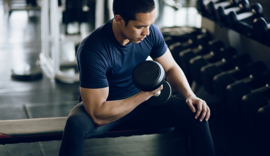 En mand sidder p en bnk i et trningcenter og lfter en vgt.