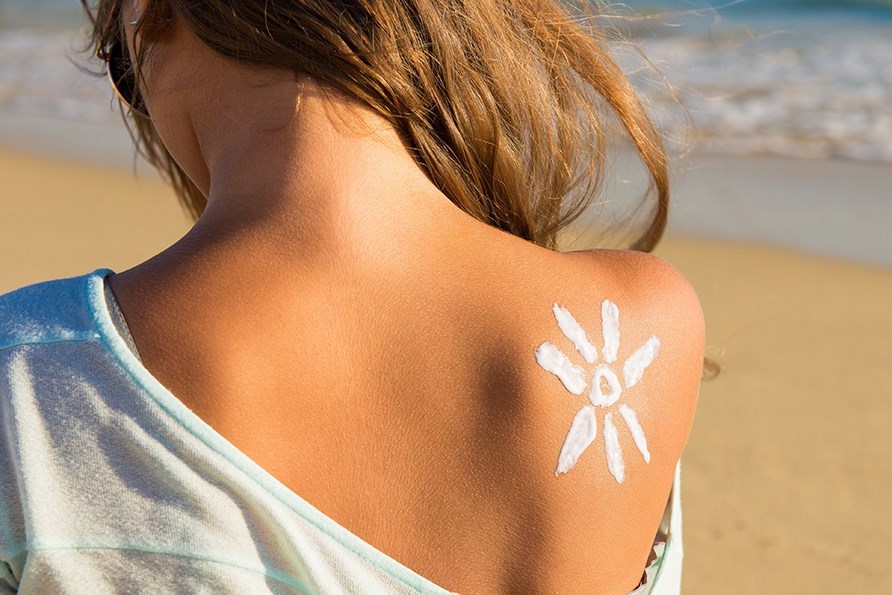 Kvinde med ryggen til kameraet p� en strand, med en sol malet p� huden i solcreme.