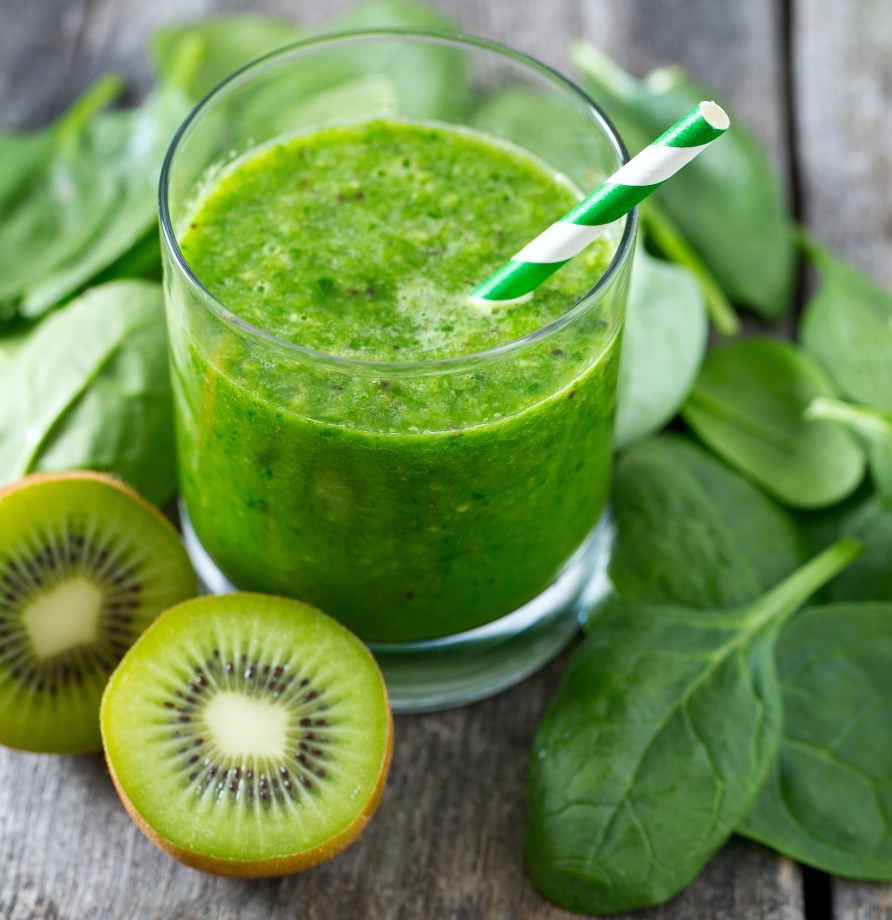 Et glas med spinatjuice, omringet af spinat blade og to halve kiwier.
