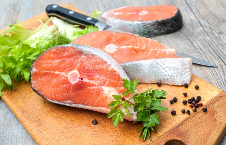 Store stykker laks ligger p et skrebrt, med friske krydderier rundt om.
