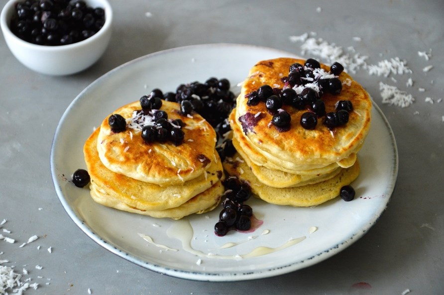 Proteinrige bananpandekager serveret med sirup, blbr og revet kokos.