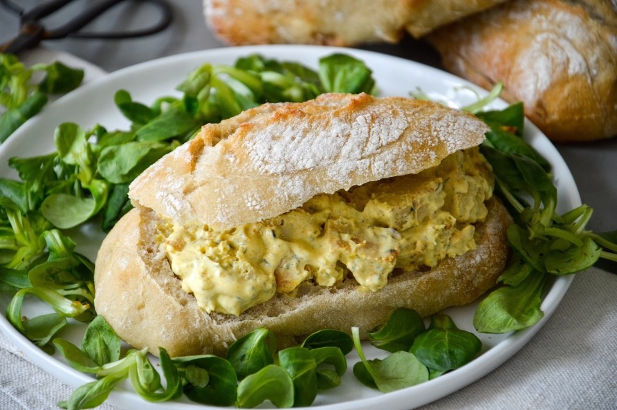 En karry kyllingesandwich ligger omringet af spinat, klar til servering.