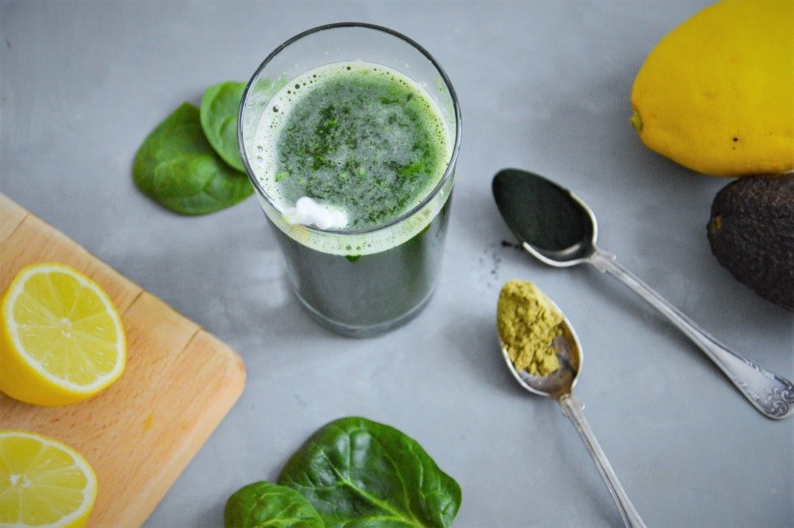 Et glas detox juice ved siden af teskeer med algepulver.