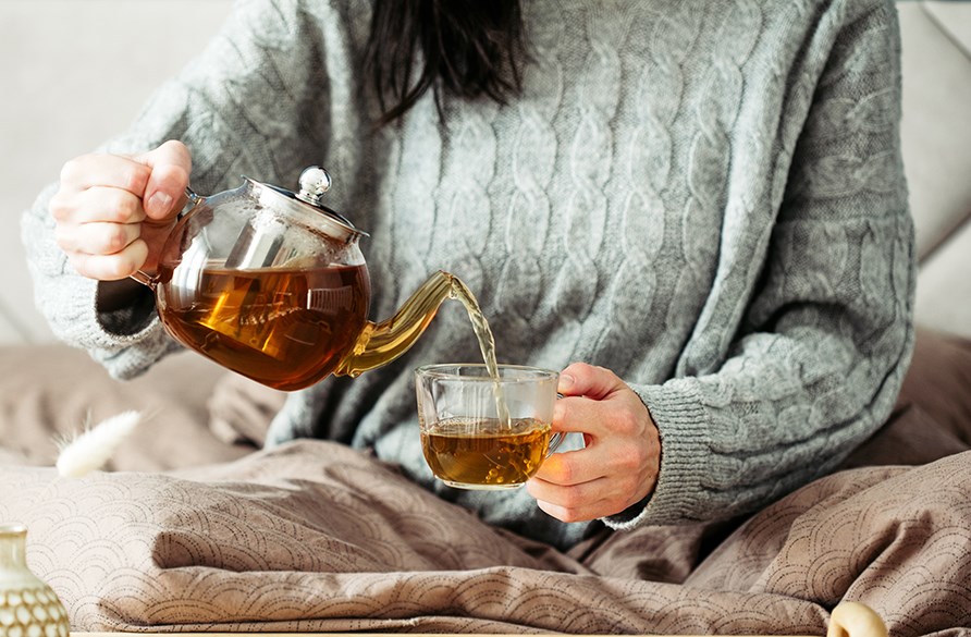 En kvinde sidder og hælder op en kop te. En kvinde sidder og hælder op en kop te.