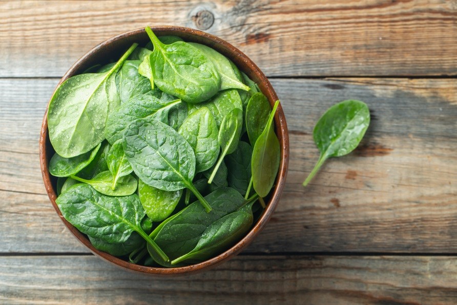 Friske spinatblade hldt i en brun skl stende p et trbord.
